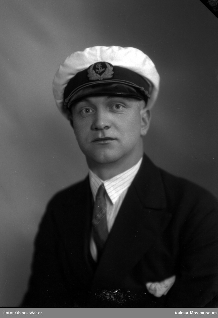 Ateljébild på en man i blazer och uniformmössa med emblem. Enligt Walter Olsons journal är bilden beställd av herr Frans Karlsson.