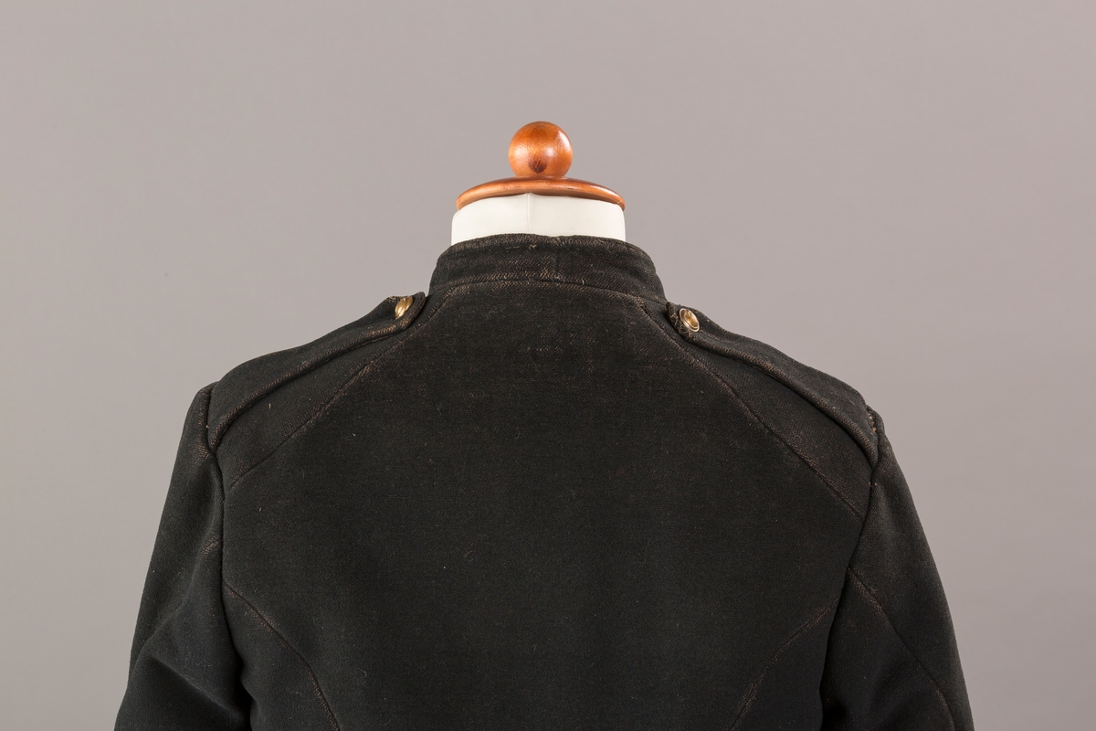 Form: Enkeltspent.

Foret med lin. Forsterket med silke på et lite stykke på ryggen. 12 messingknapper med mønster og tallet 1. Hempe i lin. Bendelbånd med knappehull.