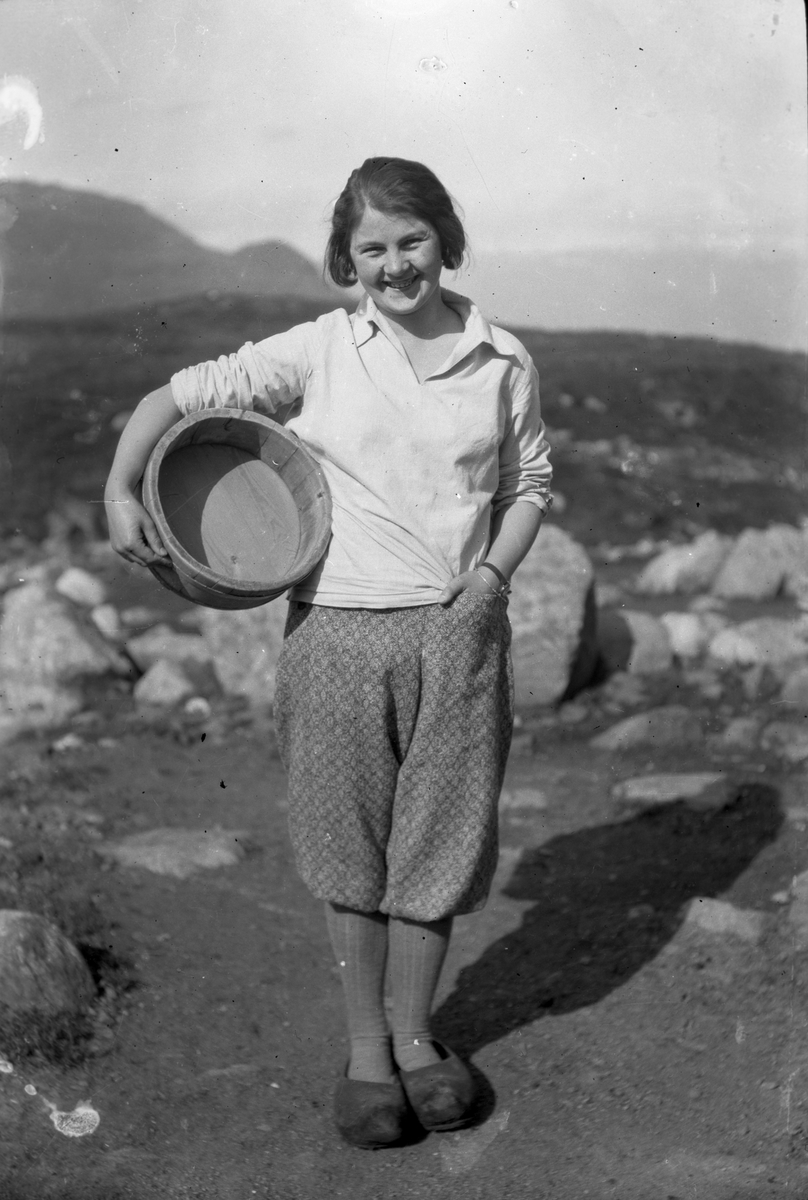 Kvinne i jumpers og knikkers med tresko på føtene og logga trebutt under armen.