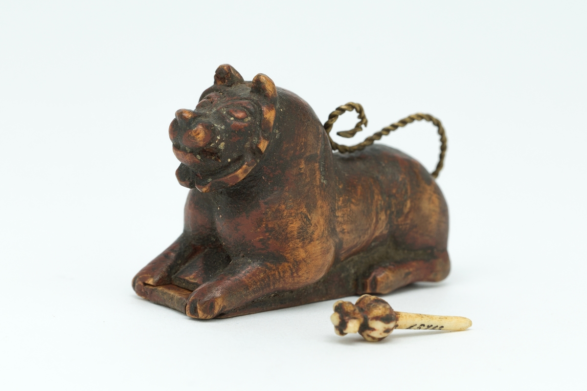 Liggende løvefigur av tre med snodd messingtrådshale. Lokk i bunnen.