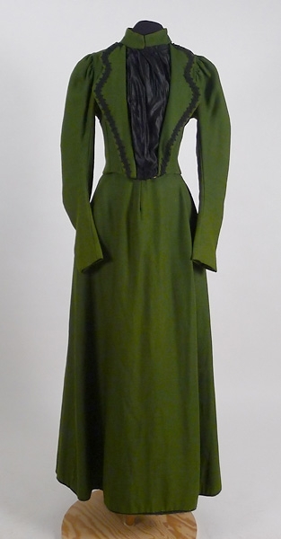 Enligt liggaren: Klänning, (klänningsliv och kjol) av grönt ylletyg med svart besättning.