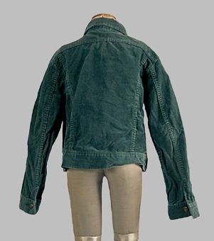 Blåaktigt grön jacka sydd av manchestertyg. Modellen är sydd med ok, rund halsringning, knäppning mitt fram samt linning längs nedre kanten. Ärmen avslutas med en linning. Runt halsringningen är en krage med spetsiga snibbar fäst. Jackan är av märket "Waquero".
Anm. enl liggaren "Tillhör 1974 års tonårsmode, men användes fram till 1977"
