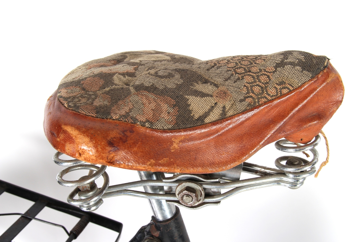 Svartlakkert damesykkel med taske til verktøy under setet og kjolenett på bakhjul. Sykkelen har Torpedo frinav.