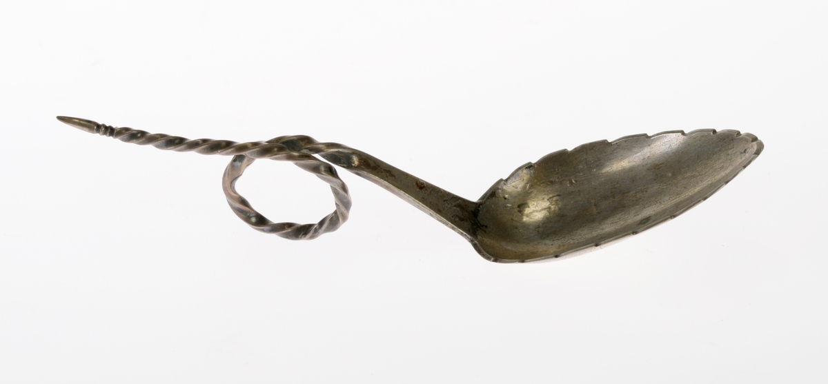 En sukkerskje av sølv. Bladet har hakk i sidene som minner om et bjørkeblad, og på undersiden er det gravert inn nerver i bladet. Skaftet er først flatt før det er snodd/tvunnet. På midten er det en løkke som fungerer som håndtak. Skaftet smalner og i enden smalner det til en spiss. På undersiden er det tre stempel. det første er en blomst som er bymerke for Trondheim. Deretter er det et monogram som viser at det er J.A. Møller som trolig har laget det. Deretter står det 13 1/2 som angir sølvgehalten. På oversiden er det gravert inn en dato.