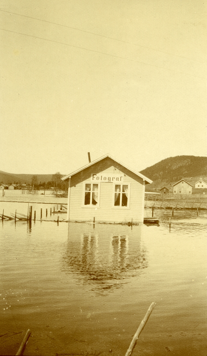 Fra flommen 1913 (?) i Innbygda, Trysil. Hus med skiltet "Fotograf" i forgrunnen. Nordby i bakgrunnen