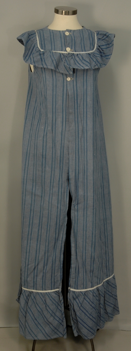 Heldekkende forkle i bomull uten ermer. Det er laget av et blågrått stoff med landsgående striper i en mørkere blå farge. Rundt halsen har det en påsydd rynket kappe i samme stoff, stoffet er skråstilt, det samme sees nederst på forkleet. Forkleet har en lomme på forsiden og åpning bak som kan lukkes med tre lerretsknapper. det er påsydd et kvitt pyntebånd over begge skråkappene og rundt lommen. På forsiden er en rift som det er bøtet på. På forkleets venstre side er et knytebånd i samme stoff som forkleet, dette mangler på høyre side.