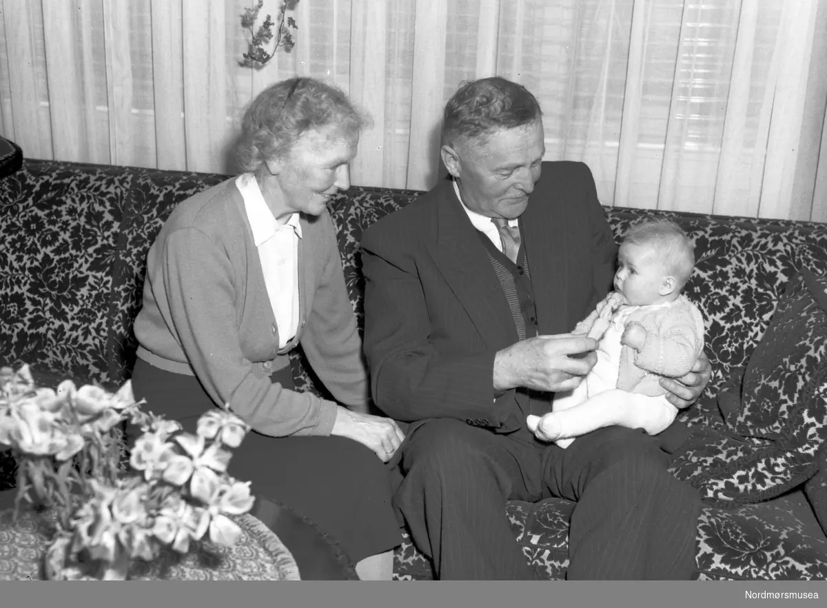 Et eldre par med en baby på fanget, kanskje er det besteforeldrene? Fra Nordmøre museum sin fotosamling, Williamsarkivet. EFR2015
