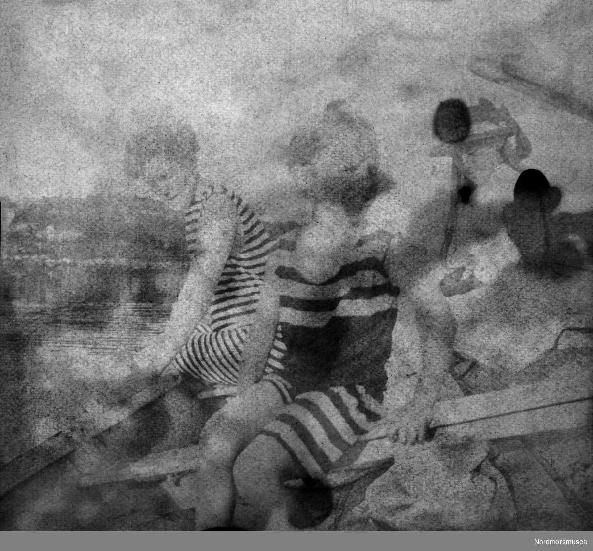 "Mamma, Hedvig og jeg i robaat paa Hasselbaken." Bildet er av særdeles dårlig kvalitet. Fra et fotoalbum tilhørende Ellinor Williams-Phakdikun (1905-1963). Fra Nordmøre museums fotosamlinger.