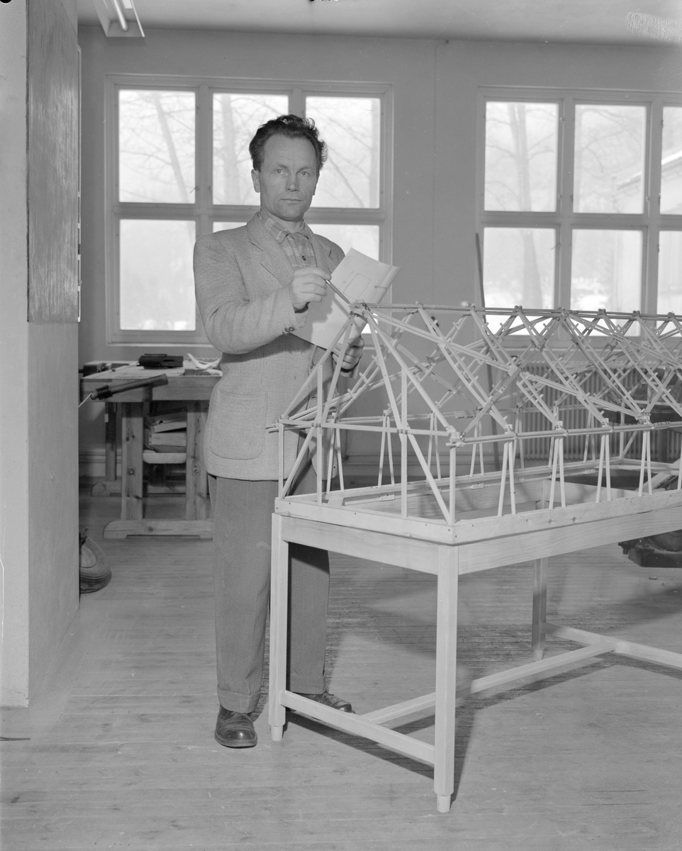 Norsk landbruks jubileumsutstilling 1959. Et blikk inn i snekkererkstedet, mann viser frem en modell, antatt veksthus.