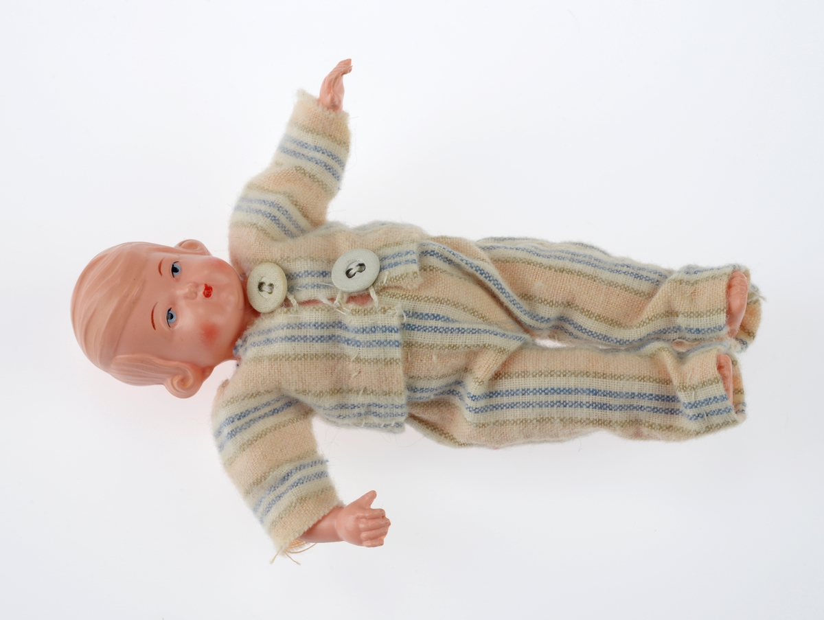 En sjokoladeeske brukt som dukkeseng med dukke, dyne, pute, skinnfell, ullteppe og madrass. Gjenstandene er undernummerert 01-08.
FTT.54432.01: En sjokoladeeske fra Freia brukt som dukkeseng. Esken er med lokk og laget av papp. Den er stiftet i hjørnene. Utenpå er det trykt julenissehoder i rødt og grønt. For tekst se "Påført tekst/merker".
FTT.54432.02: En dukke laget av plast der både armer og bein er bevegelige ved at de er festet med strikk inni dukken. Håret er støpt og er krøllet ved ørene. I ansiktet er det malt øyebryn, øyne, røde kinn og munn. Dukken har på seg en pyjamas laget av flanell. Den er stripete i fargene hvit, blå, lys oransje og grønn. På skjorten er det to knapper i fronten.
FTT.54432.03: En hodepute laget av blått bomullsstoff med heklet trekk. Puten er fyllt med diverse tekstilbiter.
FTT.54432.04: En dyne laget av blått bomullsstoff med en påsydd blondekant foran. Baksiden er sydd sammen av tre ulike tekstiler. Dynen er fyllt med tekstilbiter.
FTT.54432.05: En brunsvart skinnfell, trolig laget av kaninpels.
FTT.54432.06: Et ullteppe som trolig klippet ut av et eksisterende ullteppe. Teppet er gulhvitt med blomster og blader i rosalilla.
FTT.54432.07: Et sammenbrettet stykke som er heklet. Trolig en rest som er brukt som madrass i esken/sengen.
FTT.54432.08: Et sammenbrettet stykke som er heklet. Trolig en rest som er brukt som madrass i esken/sengen.