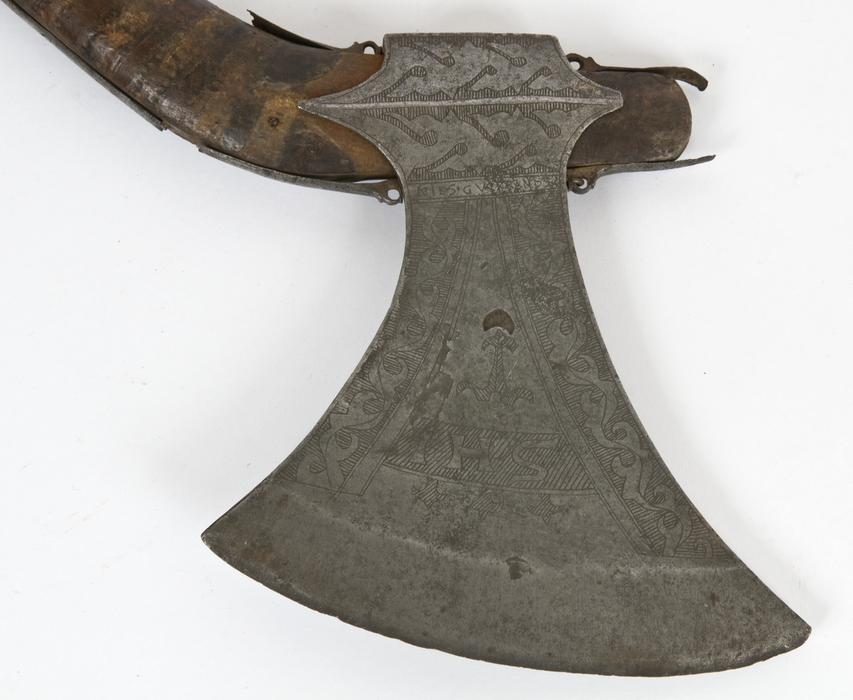 Asymmetrisk blad med lang øvre spiss og kortere nedre spiss. Bladet er klieformet. med påsmidd egg- Øksen har stset dekor på begge sider. Øksen er merket med IHS på begge sider  Skjellmønstet smedmerke på utsiden. Innskipsjon på utsiden NILS. G VIKRANDSØN  På innsiden ANNO 1634
Øksehammeren har skaftehull og skinner.
Gammelt skaft med jernskinner og rester/ av / merker etter bånd..Skaftet har doppsko med pigg og fire fliker med ringer på enden.
Skaftet er krummet.