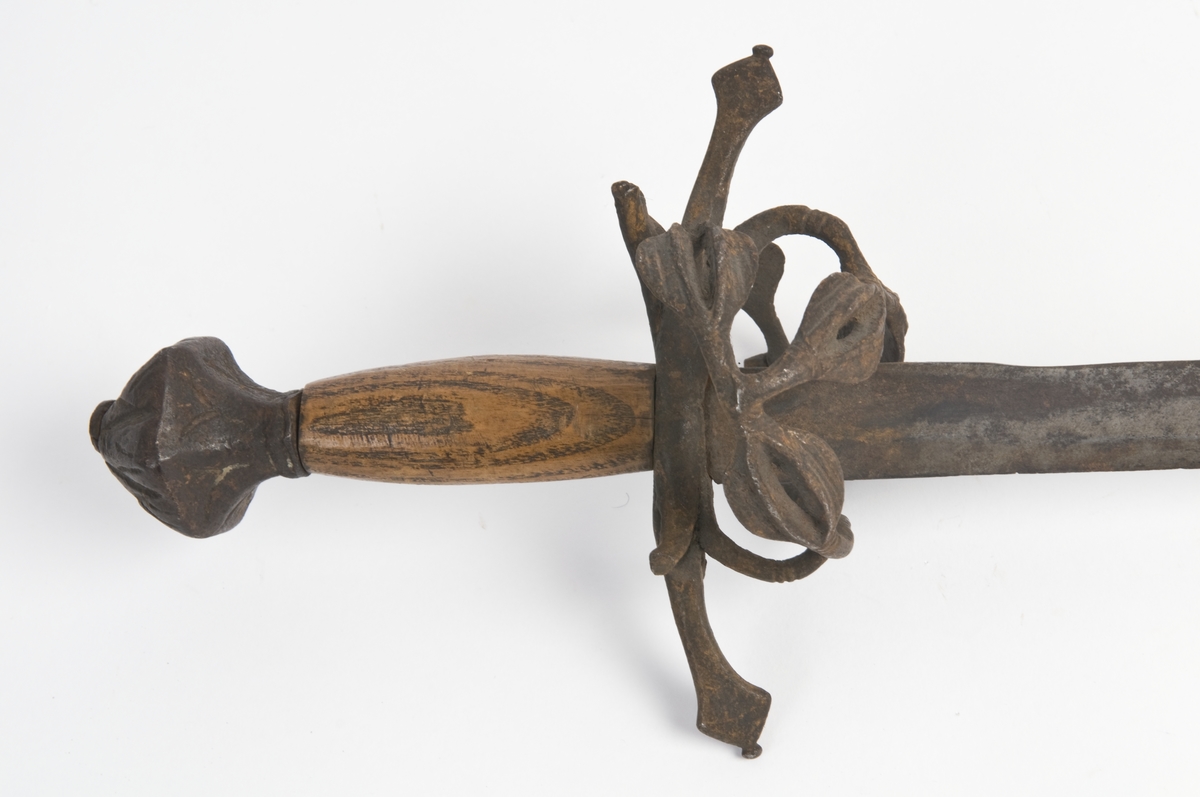 Kjegleformet 6 kantet knapp med nitteknapp og smidd bladdekor. Tregrep Øvre del av festet msgnler. Rette parerstenger med rombeformede avslutninger.
Rett tveegget klinge med kileformet  tverrsnitt og ryggslipning mot spissen