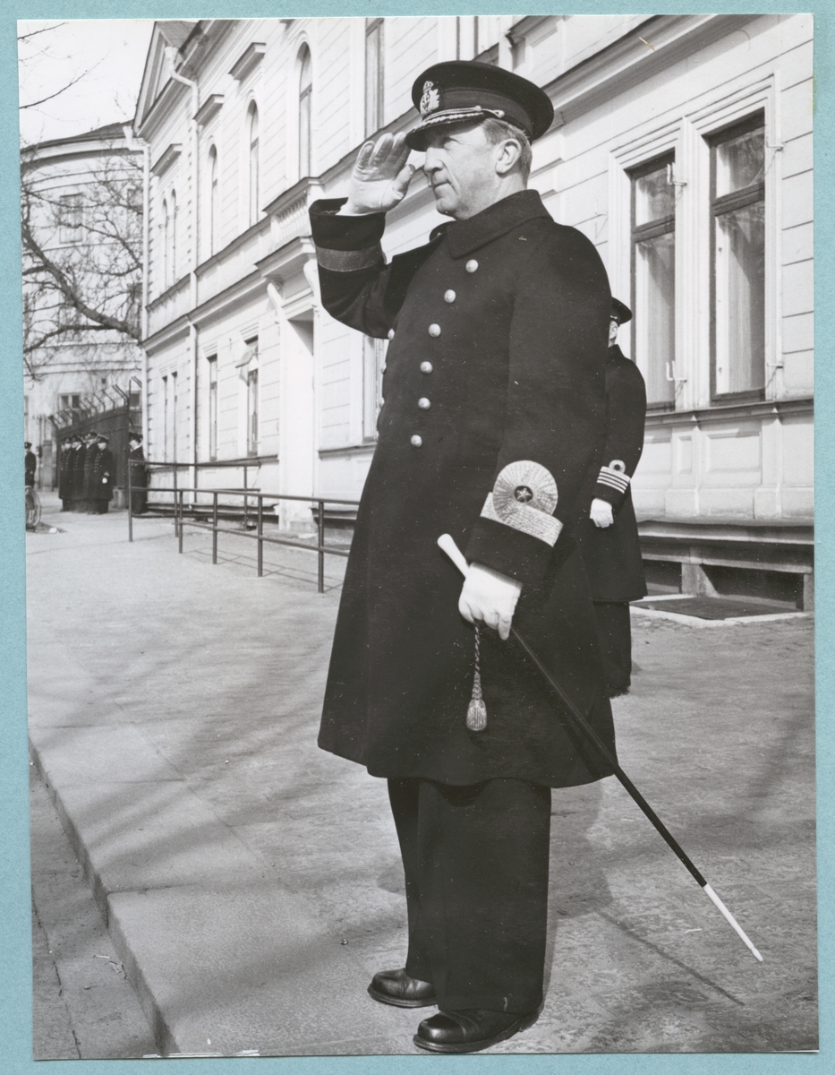 Konteramiral Samuelson, klädd i uniform, står utanför bataljon Sparres kanslihus och gör honör. Fotot är daterat till 17-3-1952.