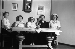 Fem personer avbildet ved et bord. Lengst til høyre sitter E