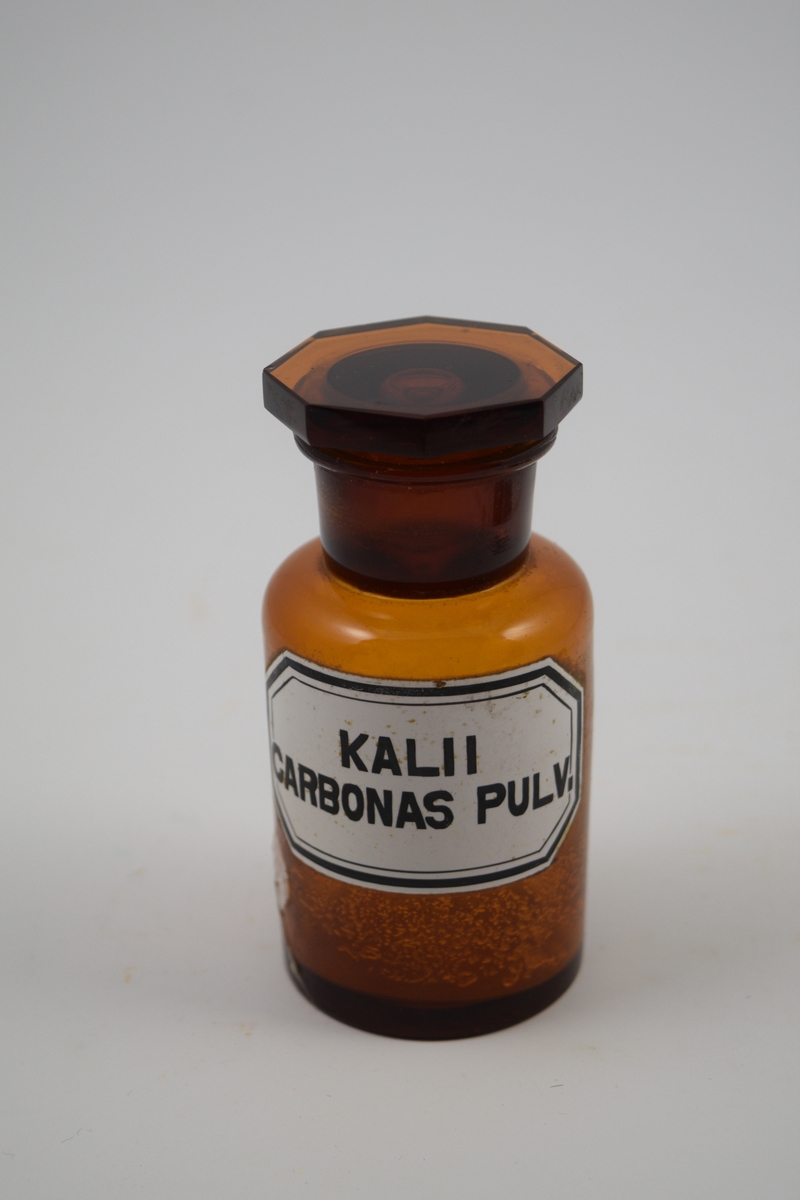 Brun glasskrukke med glasspropp. Kalii carbonas pulv. brukes til produksjon av legemidler.