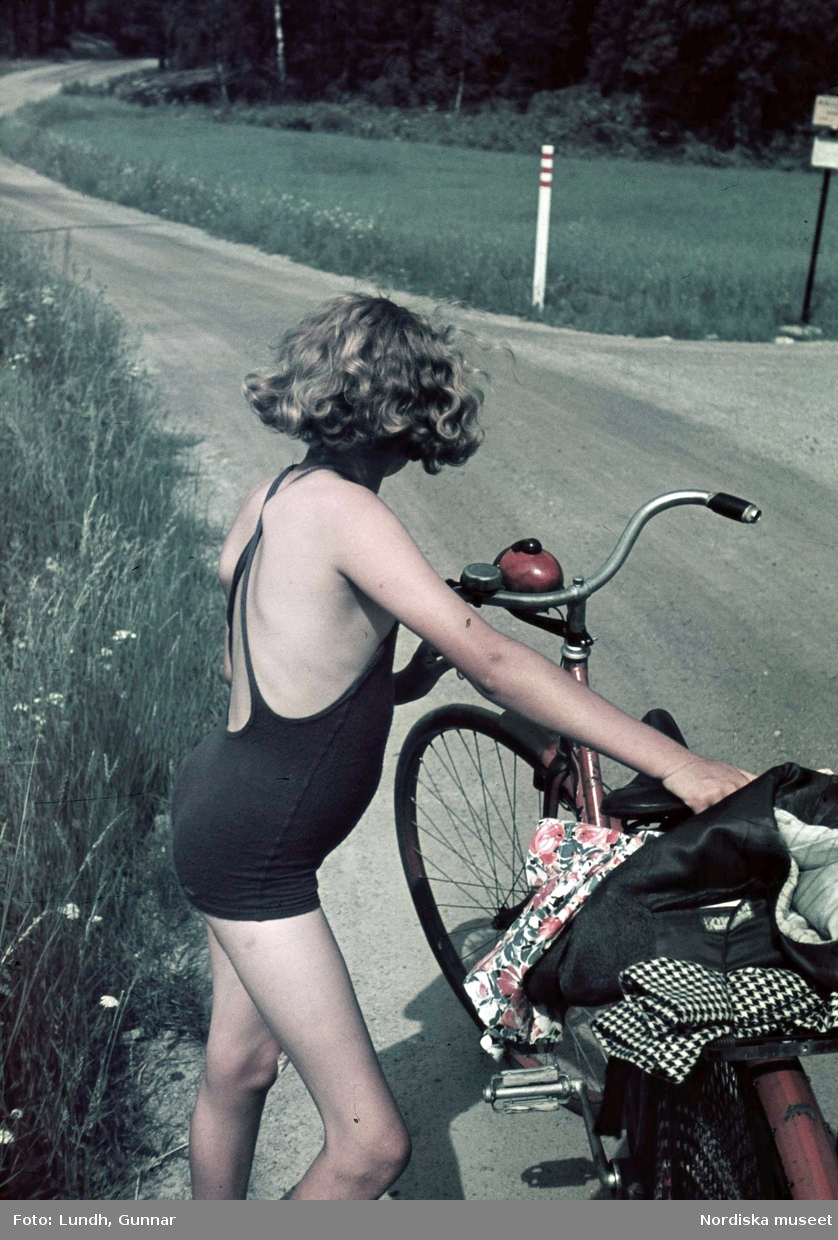 Flicka, fotografens dotter Jytte, i blå baddräkt med cykel. Troligen fotograf Gunnar Lundhs dotter Jytte.