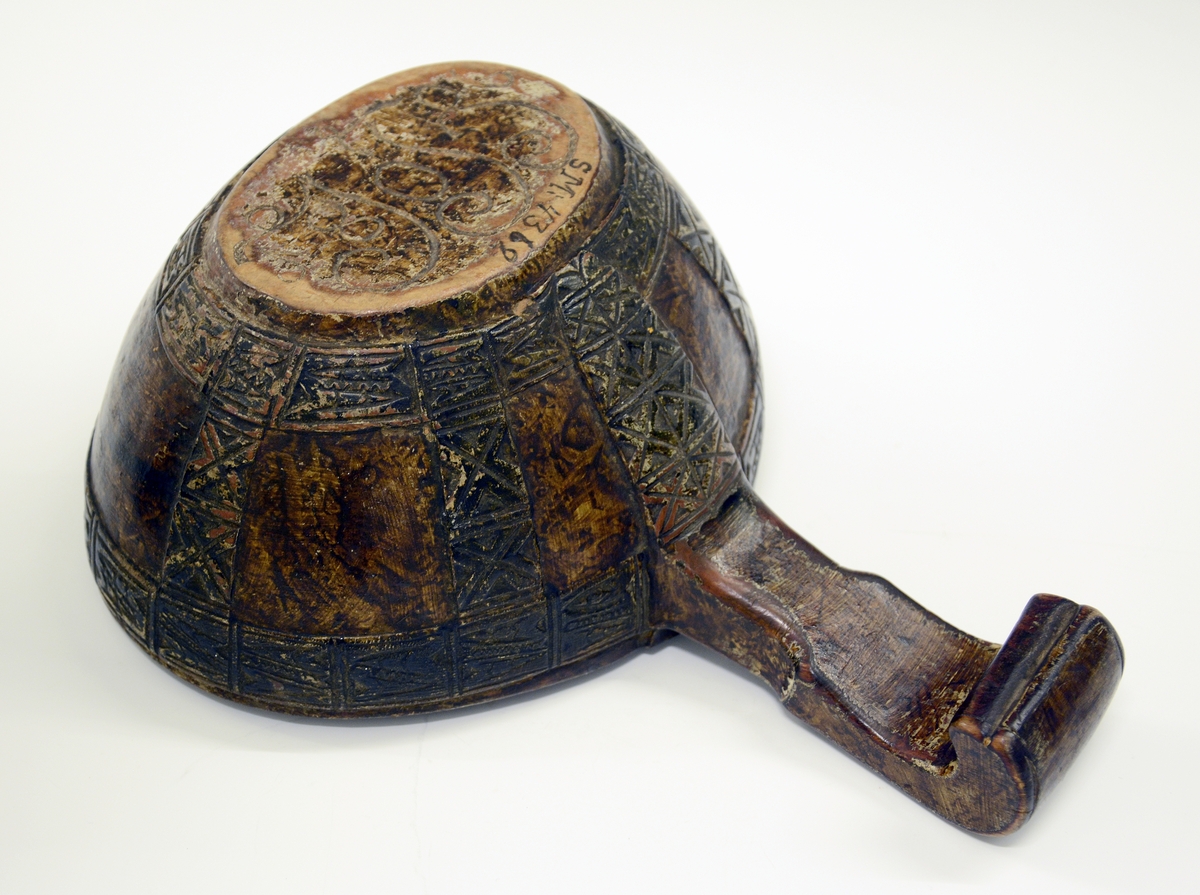 Øløse i tre. Fra protokollen: Øse fra 1806. Under bunden skaaret JTS 1806. Bladorn. paa skaftet. Utenpaa baand av kerbsnitruter, indelt i 4 kanter. Rundt kanten oppe, nede og 5 paa tvers og ett dobbelt ved skaftet.