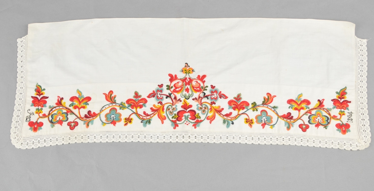 Kinnlag i kvitt linlerret, utsauma med ullgarn ("kamelgarn"), i raudt, grønt, gult, blått, orange og svart. Borden er sauma gjennom dobbelt tøy. Påsydd kvit bomullsblonde på tre sider, jarekant på kortsidene og falda på langsida.