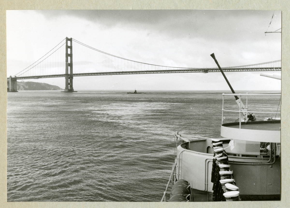 Bilden föreställer Golden Gate-bron i San Francisco. På bilden syns även en del av minfartyget Älvsnabben och ombord en rad besättningsmän i uniform. Bilden är tagen i samband med fartygets långresa 1966-1967.
