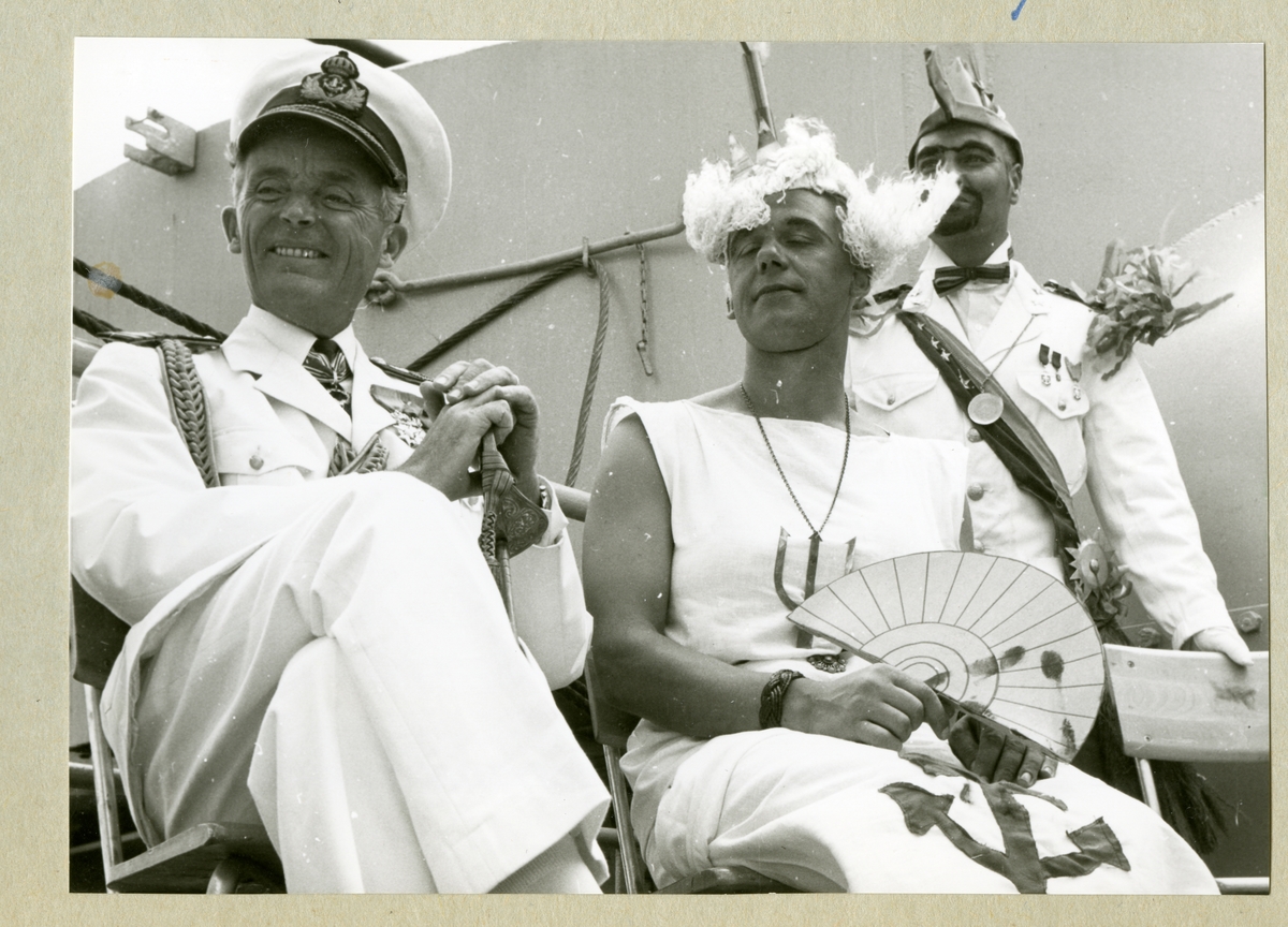 Bilden föreställer en man i uniform och två utklädda män i samband med ett linjedop ombord på minfartyget Älvsnabben under långresan 1966-1967. En av de utklädda männen ska föreställa kung Neptuns drottning.