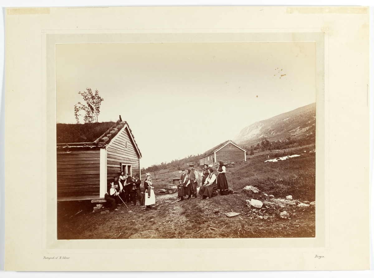 Brudesyning på Gjerdetunet, Straumgjerde, Sykkylven ca.1862. Personer med brud i sentrum på tun med inn- og uthus, med klestørk utover på bakken i bakgrunnen.
Brudeparet er Elling P. Strømmegjerde og Louise Hansdtr. Fet.