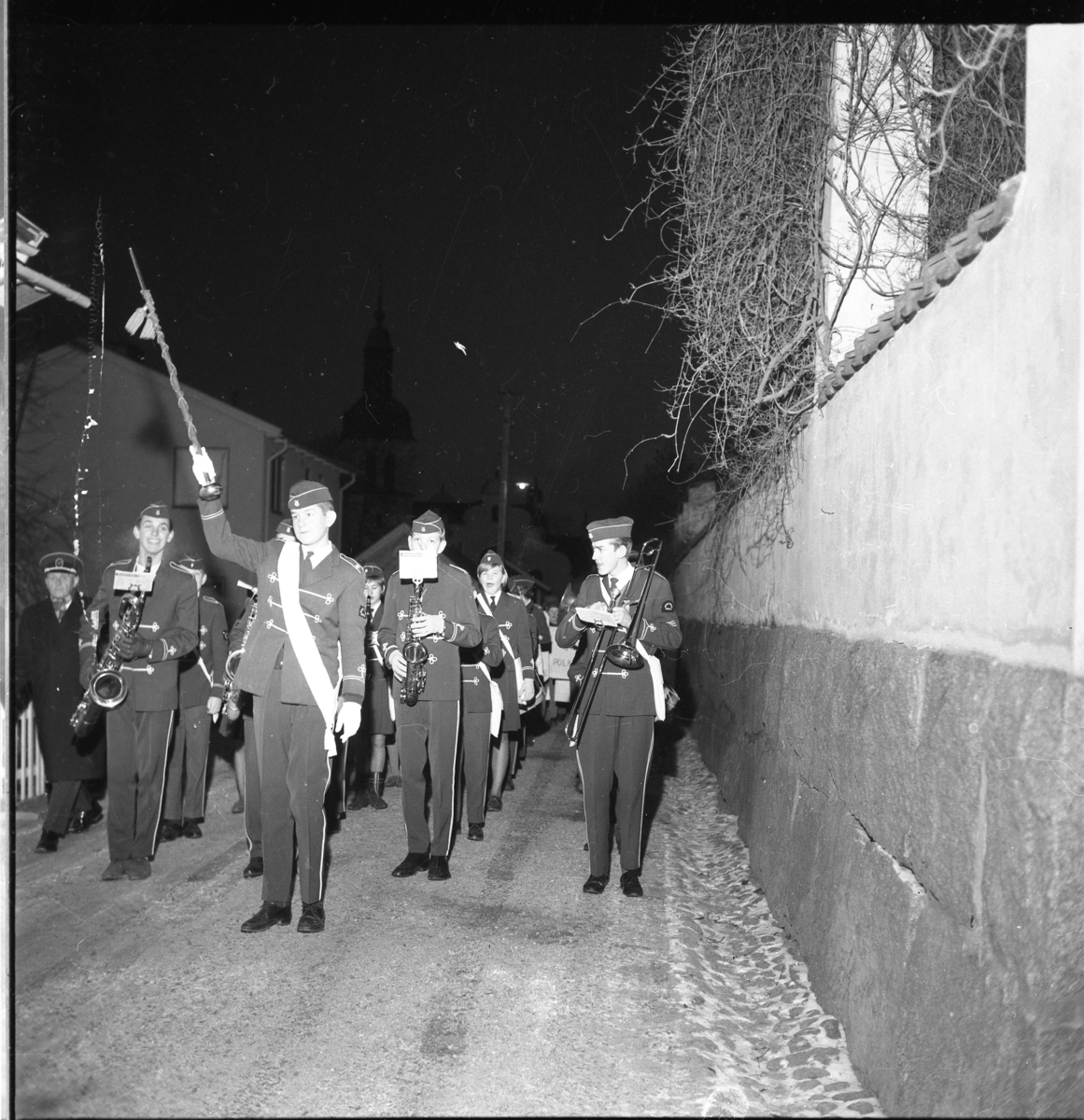 Okänd musikkår marscherar och spelar på Bergsgatan i Gränna, mellan kyrkan och Södra parken, i samband med Lucia 1963.