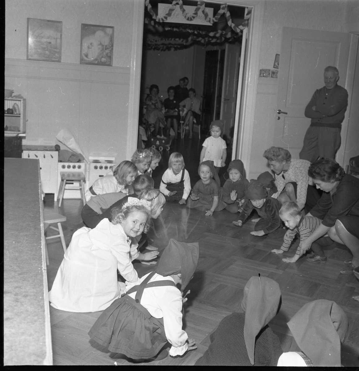 Lekskolan i Gränna, jultid 1963. Okända barn och vuxna sitter i en ring på golvet.