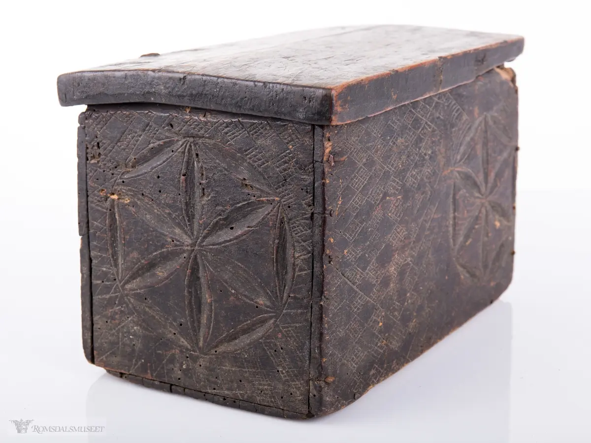 Seksbladsroser i karveskurd. 2 bak, en i front og en på hver korside. Rissede dekorfelt omkranser motivene.