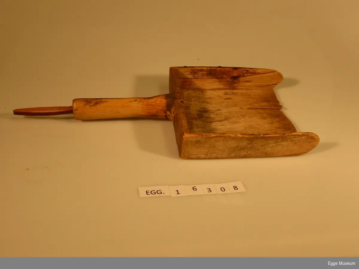 En spade laget av tre. Kan være brukt som melspade eller feiebrett. Den har en hemp av lær i håndtak.