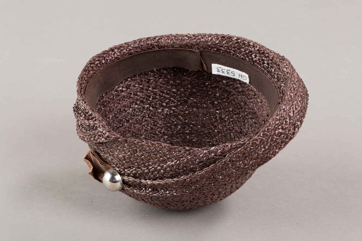 Form: Sirkelformet, avrundet  med brem og lita silkesløyfe med knapp. Bomullsbånd innvendig
Brem oppbrettet i spiralform med bredde økende til avslutning hvor den er festet til pullen med en plastknapp og sløyfe