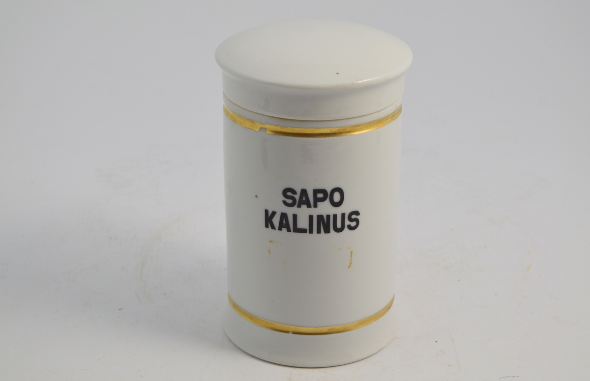 Sylinderformet porselenskrukke med porselenslokk. Hvit med gulldekor linje langs toppen og bunnen. Påtrykket med sort skrift SAPO KALINUS som er en Kalisåpe. Krukken blir brukt til oppbevaring av kalisåpe, også kalt medisinsk såpe.