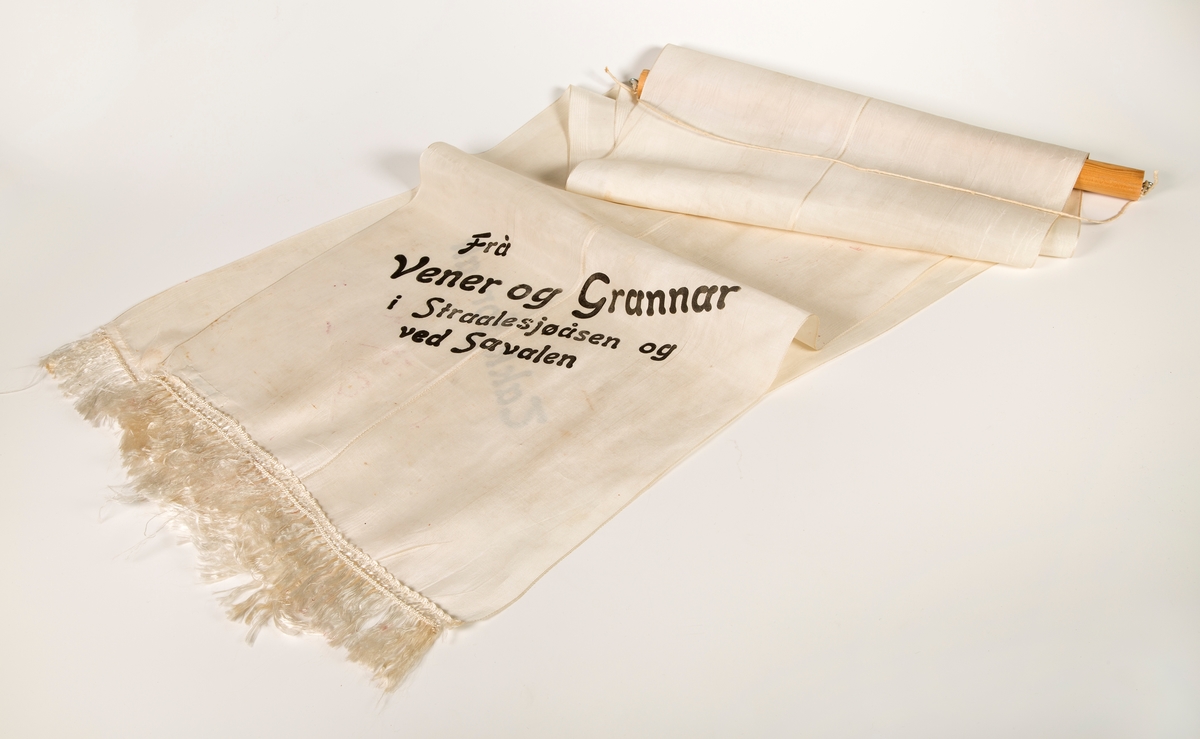 Stort sørgebånd til begravelse. Festet til rundstokk for oppheng på vegg. Til Garborgs begravelse.