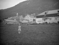 Sygard Forr med ei lita jente som står utpå jordet i forgrun