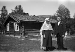 Brudeparet Marie og Hans Kleiven ved en tømmerstue. Hun har 