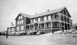 Grotli Høyfjellshotell med folk og biler parkert.