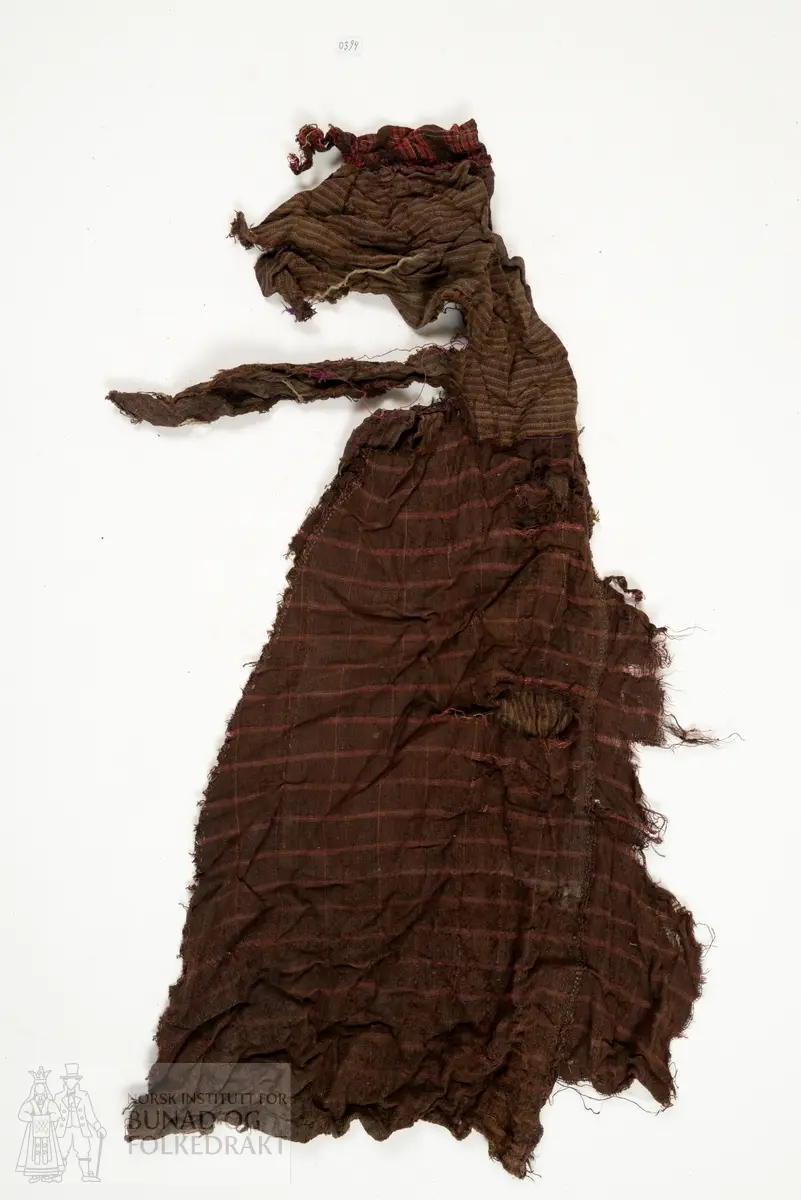 Svært utslitt del av ein stakk med linning, nederkant og ei metallhekte i eine enden av linning. Nedanfor denne delen av linning er det sauma fald som truleg er splitten midt framme på stakken. Av tre ulike verkensstoff, lerretsbinding med bomull i renning, ull i innslag. Stripete stoff i brun og lilla, svært utydeleg lillafargar. Fleire små hol etter mus, har vore nytta som stappefille.