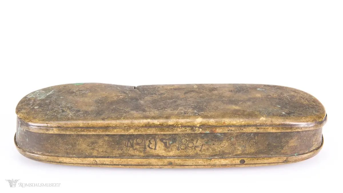Rektangulær messingeske med avrundede ender. Har en påsatt og påklinket utenpåliggende bunn og utenpåliggende, hengslet lokk