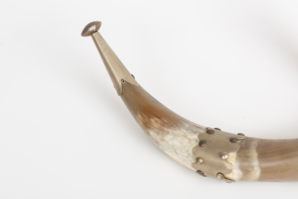 Knaggrekke antagelig håndlaget av kuhorn. 4 horn/kangger. Montert med "dekorative" beslag som er spikret og dekornaglet på hornene. Kledd med cordfløyelstoff på midtparti. To øyeskruer på toppen for feste til vegg.