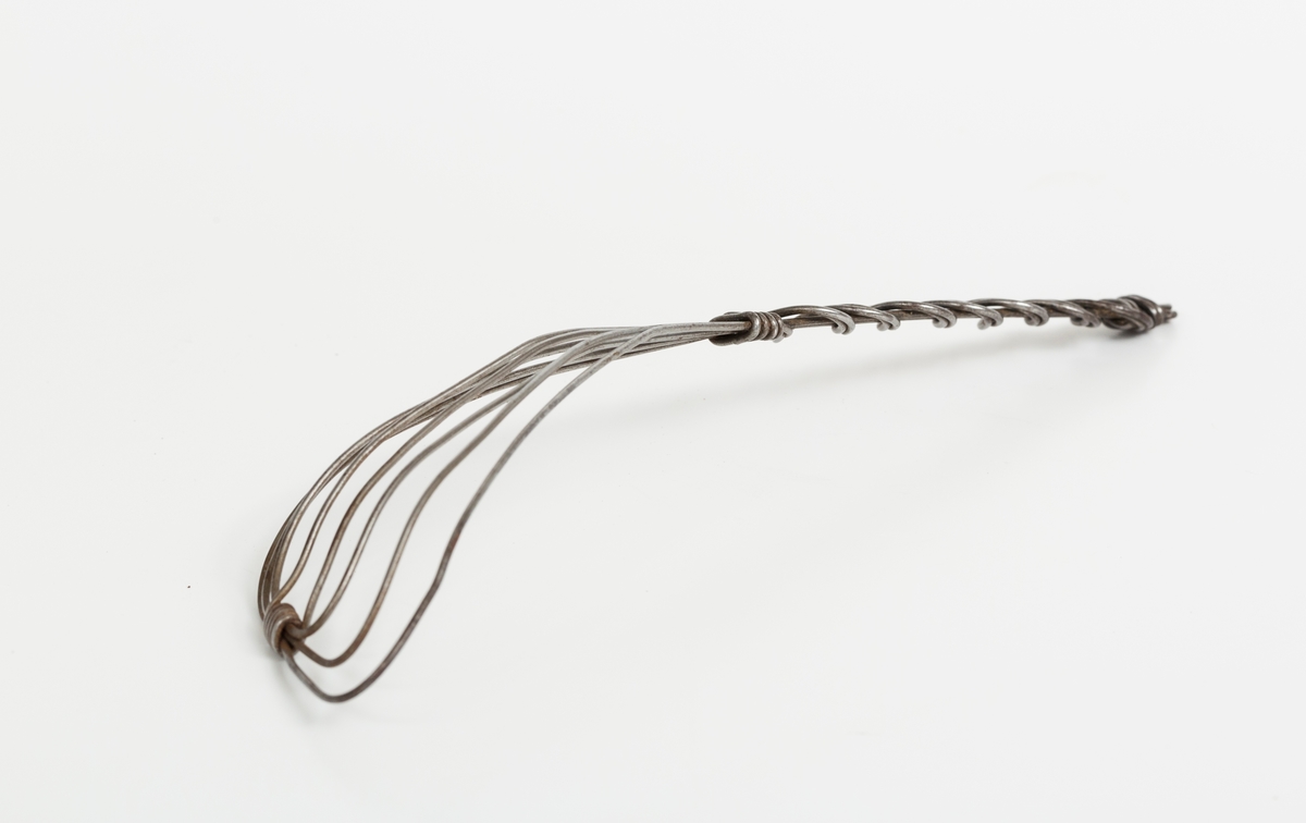 Visp i ståltråd. Bøyd spadeformet del med håndtak. Trådene går i løkker som vekselvis danner spade og håndtak. Håndtaket er samlet med omslynget tråd i en slags ornamental form.
