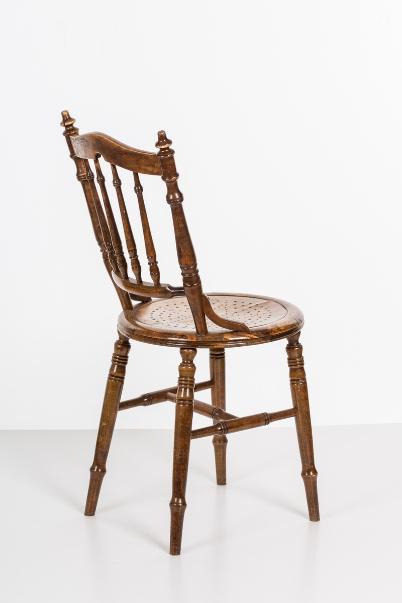 Stol i lakket treverk. Rundt stolsete med hullemønster. Rygg som er svakt buet med spiler og mønster. Dreide ben og spiler i rygg.