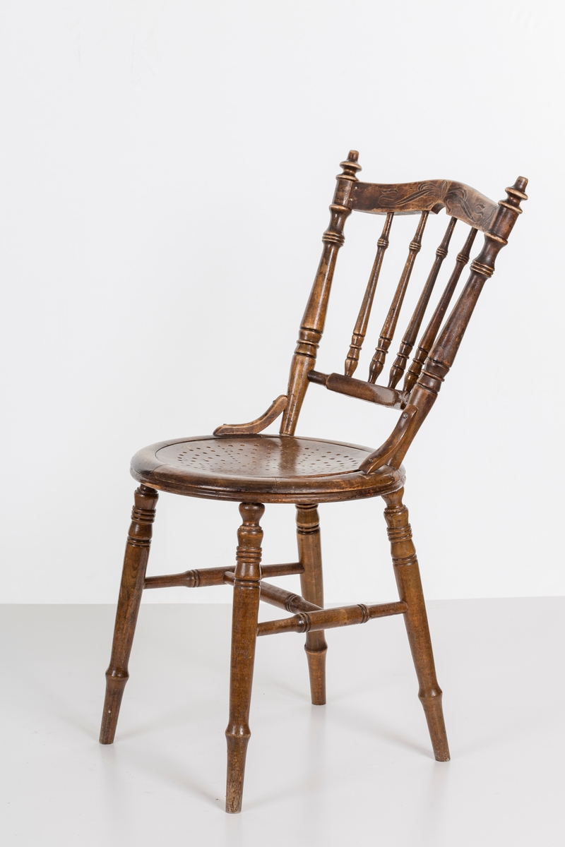 Stol i lakket treverk. Rundt stolsete med hullemønster. Rygg som er svakt buet med spiler og mønster. Dreide ben og spiler i rygg.