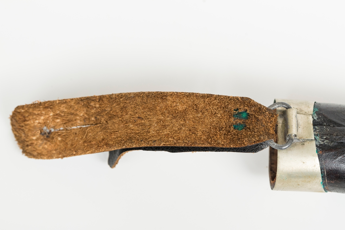 Håndsydd lærslire med holker oppe og nede. Slire og stropp av separate lærstykker. Sliren har enkel  pautet dekor. Holkene er håndloddet nysølv (sansynligvis) med enkel trambulert dekor. Toppholken har påloddet hengsle og D-ring til feste for slirestropp.