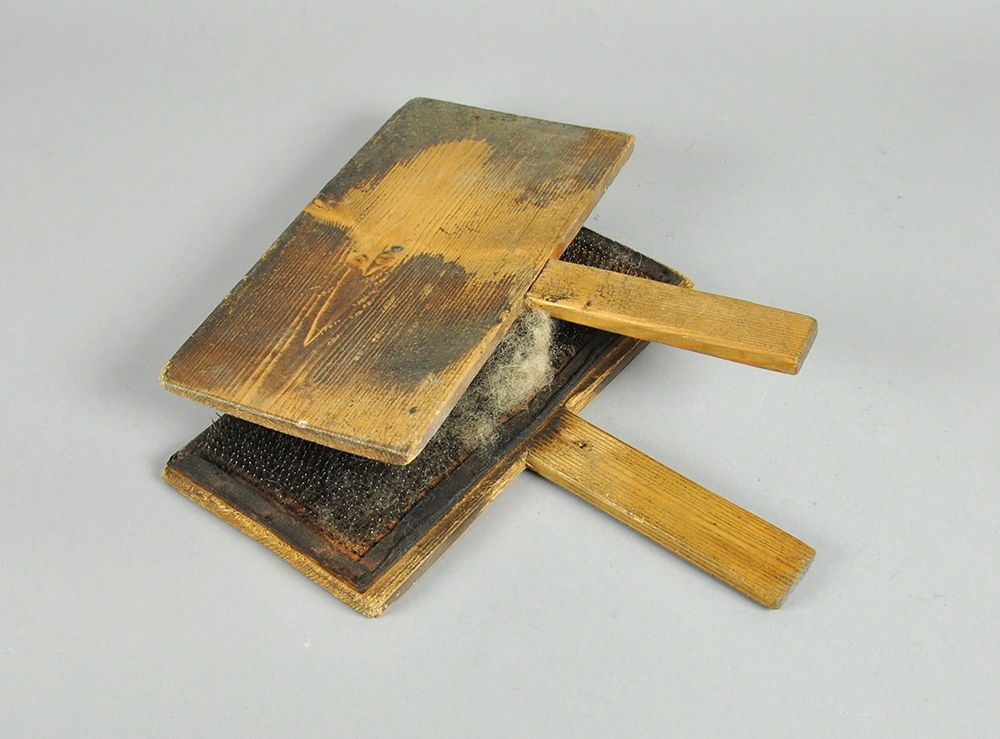 To treplater hvor innsiden av begge platene er dekket av en skinnduk med tettsittende nåler. Begge treplatene har håndtak.