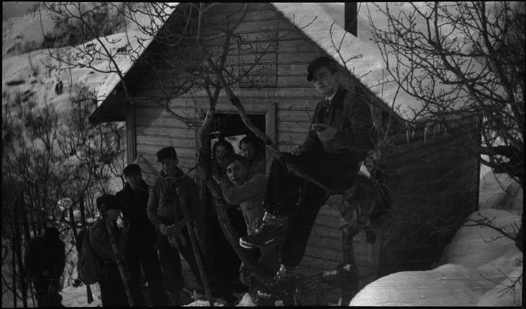 En gjeng gutter, unge menn og kvinner i godt humør med ski på beina utenfor en hytte. Det er også bilder fra en bakke med en stor folkemengde som ser på folk som kjører utfor med staver som porter.