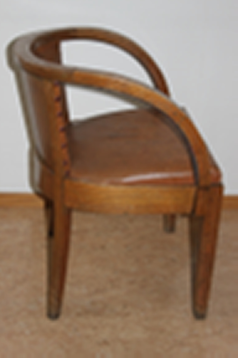 Møteromstol/kontorstol med armlener samt buet rygg. 4 ben. Metallbeslag under armlener. Brunt skinn i rygg og sete. Stolen er lakket med klar lakk. Originalt møbel innkjøpt til det nye Statsarkivet i Kristiansand i 1935.