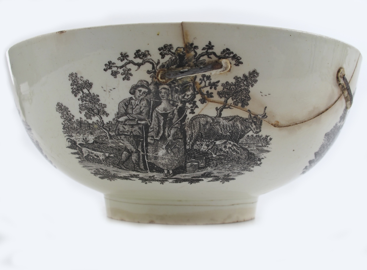 rundt siden 4 bonderomantiske landskaper: Gjeter og budeie  m. ku, Ku, der drikker i et vann; båt, vann og vind mølle;  Bonde der vasser over vann mot bondegård med sine to kuer; Beitende ku m. kalv, spaserende personer,  samt flod og hus i  bakgrunnen; innvendig i bunnen den  forelskede budeie  med sin gjeter i noe forstørret målestokk;