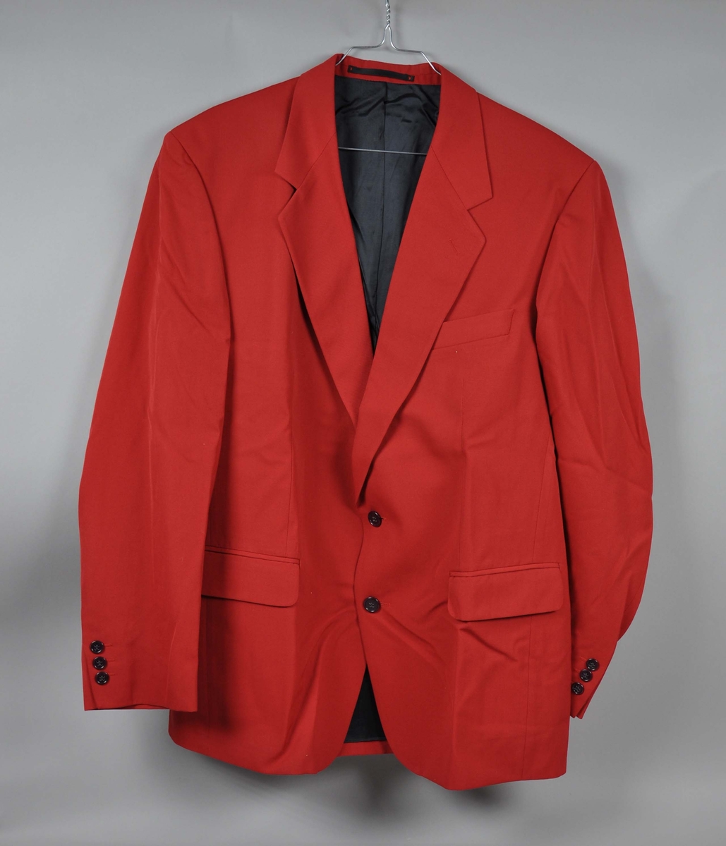 Rød ullgabardin-jakke , toknappet med en skrå brystlomme og to lommer med klaff. Tre innerlommer.
Mørkeblått for i viscose.