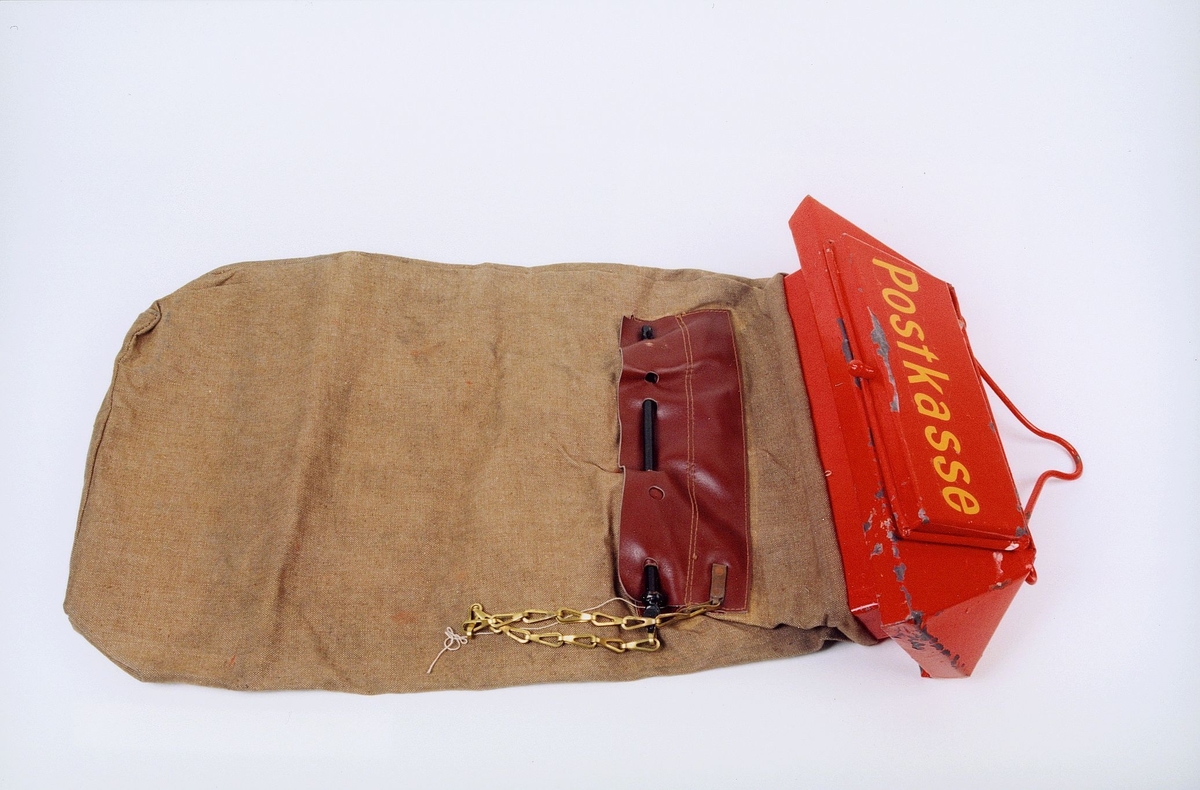 Rødt beslag med med ordet "Postkasse" og med oppheng. Sekkebeholder i strie.  Skinnkledd tømmeåpning med låseanordning.
