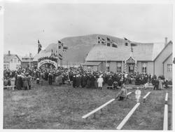 Folk, flagg og bygninger på Melbu. Til venstre et skilt med 