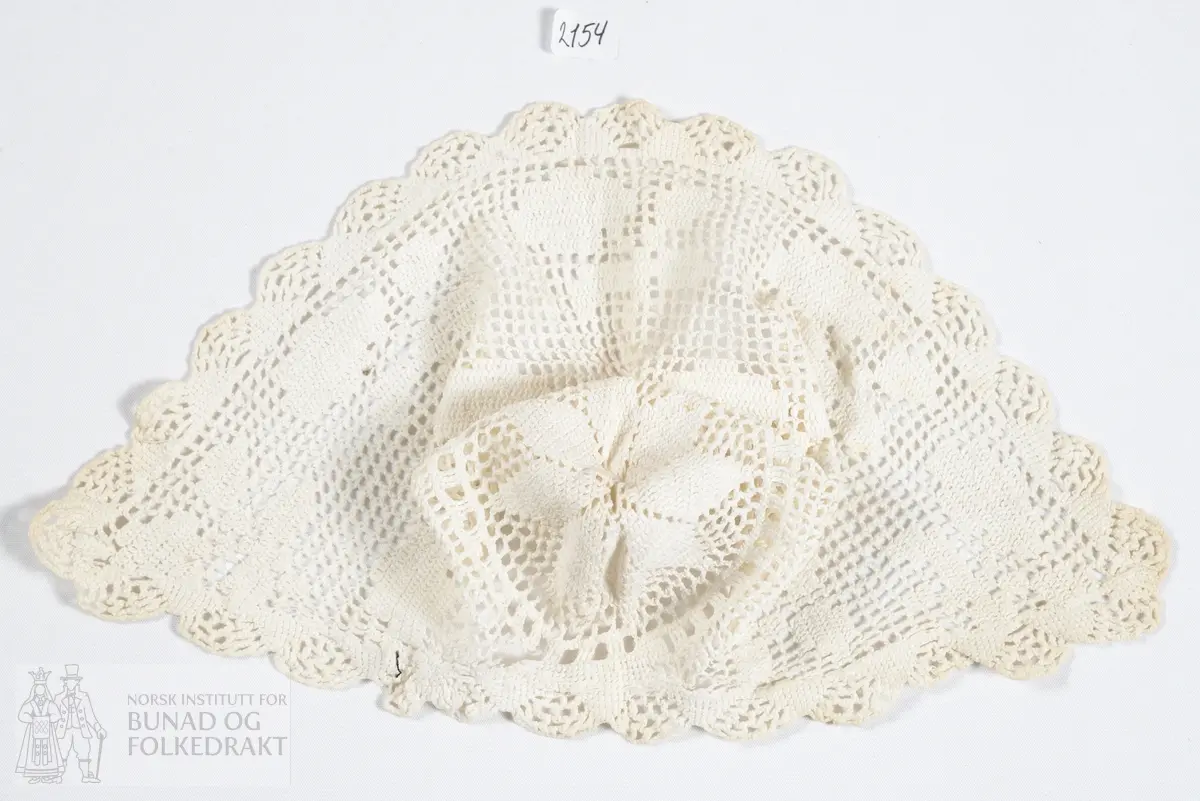 Barnelue. Heklet av hvitt bomullsgarn. Mønsteret ender i en stjerne i bakhodet. Kantet med tungekant rundt hele.